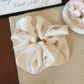 Close-up of champagne silk scrunchie with luxury texture and a gold metal logo charm - Off White