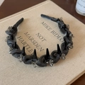 Detail van grijze mesh hoofdband met zwarte spikes en kristallen op een boekoppervlak - Grijs Gaas