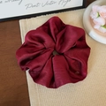 Close-up of wine red satin scrunchie with smooth texture and small round metal pendant - Red