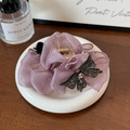 Détail d'une pince à cheveux en satin rose poudré avec nœud en strass noir sur plateau - Rose