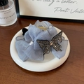 Vue détaillée d'une pince à cheveux fleur bleue avec un papillon en strass sur plateau céramique - Bleu 11cm