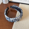 Detailed view of the wide blue and white ink print braided headband on a wooden table - Light Blue Floral