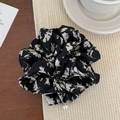 Detail of floral chiffon scrunchie with delicate pearl pendant on a soft beige fabric background - Black Printed