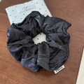 Detail of glossy black satin scrunchie with FMdrea label on a dark wooden surface - Black