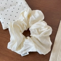 Detail of a creamy beige silk-like scrunchie with brand label on a dark wood table - Off White
