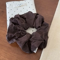 Close-up of a glossy dark brown scrunchie with soft fabric texture on a rustic wooden desk - Brown