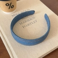 Nahaufnahme eines blauen Denim-Haarreifens mit orangefarbenen Nähten auf einem Buch - Denim Mittelblau