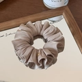 Detail of light brown silk scrunchie with golden metal logo on a wooden mirror - Champagne