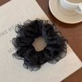 Detailed shot of black polka dot hair scrunchie with lace trim on a beige fabric book - Black