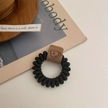 Nahaufnahme des schwarzen Spiral-Haargummis mit braunmis mit braunem Filz-Smiley-Anhänger im Detail - Schwarz