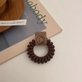 Detailaufnahme des braunen Spiral-Haargummis mit Smiley-Anhänger auf Ästhetik-Hintergrund - Braun