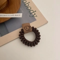 Nahaufnahme eines braunen Telefonkabel-Haargummis mit Leder-Smiley-Anhänger-Detail - Dunkelbraun