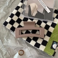Detail view of a matte brown rectangular hair claw clip on a stylish checkered knit surface - Rectangular Hollow Style / Square Khaki