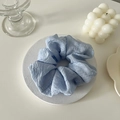 Détail d'un chouchou bleu clair à texture plissée sur un support d'exposition minimaliste - Bleu