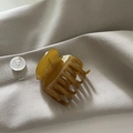 Détail d'une pince à cheveux en acétate ambré sur tissu beige avec une finition brillante - Petit Jaune