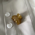 Détail d'une pince à cheveux ambre translucide posée sur un tissu de blazer beige - Vert Jaune Éventail