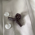 Detail of a glossy dark coffee cross claw clip pinned on a beige fabric jacket collar - Dark Gray Cross