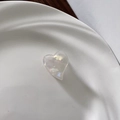 Macro detail of heart-shaped acetate hair clip with iridescent pearl finish in a ceramic bowl - White