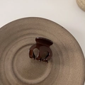 Detalle de una pequeña pinza para el pelo de acetato ámbar sobre plato cerámico - Café Oscuro