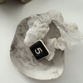 Detail eines cremefarbenen Spitzen-Scrunchies mit Häkelstruktur und schwarzem Anhänger - Spitze Nummer 5 Dekoration (5 Zi) / Gebrochenes Weiß