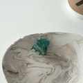 Close-up of a mini hair claw clip with dark green marble texture and golden logo - Cyan
