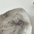 Close-up of a silver metal smiley face hair claw clip on marble tray with brushed texture - Trapezoid Silver
