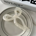 Detail of a creamy white translucent bow hair claw clip placed on a white decorative plate - Champagne