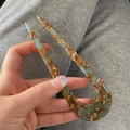 Close-up of tortoise shell U-shaped hair pin in blue and amber resin held in hand - Green & Brown