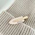 Vue détaillée de la pince à cheveux en acétate rose et doré avec logo sur fond en tricot - Blanc Lait