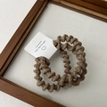 Detailed macro view of brown spiral elastic hair ties on a white display card in a wooden tray - Khaki