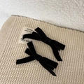 Detalle de elegantes horquillas con lazo de terciopelo negro sobre fondo beige tejido - Negro
