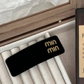 Detail view of golden min letter stud earrings on a premium black velvet display card - Rectangle Style / Black