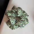 Détail d'un chouchou en satin à imprimé léopard vert fruit avec des taches roses - Vert