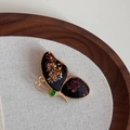 Detailopname van een vlinderbroche met goudborduurwerk en groene edelsteenaccent - Zwart