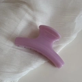 Close-up of a glossy lavender resin hair claw clip on white pleated fabric texture - Purple