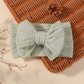 Elastic light green baby headband with large ribbed bow on a natural woven basket - Light Green