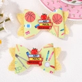 Detail showing school-themed hair clips with book and apple charms on green printed fabric - Green Books School Style