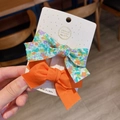 Detail of handmade bow hair clips with floral and solid orange fabric on display card - Orange
