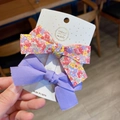 Detail of two handmade bow hair clips with pink floral and solid purple fabric textures - Purple