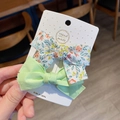 Detail view of two handmade floral and mint green bow hair clips for women on a card - Green