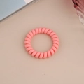 Detail view of pink matte spiral telephone wire hair tie on a decorative desk setup - Matte Peach