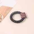 Élastique spirale noir mat avec étiquette en tissu marron et motif smiley sur fond rose - Étiquette Sourire-Noir