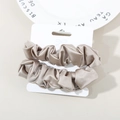 Set de coleteros elásticos de satén en color champán sobre un plato decorativo blanco - Gris Cálido