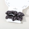 Two-pack dark grey satin scrunchies set on white retail display card with elegant props - Dark Purple