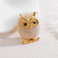 Détail macro d'une broche chouette dorée avec perles blanches sur branche métallique - Hibou / chouette