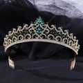Close-up of golden crown with intricate hollow patterns and dark green crystals - KC Gold With Green Rhinestone