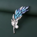 Detalle de broche de espiga plateada con cristales azules y perla sobre fondo verde - Azul Plata