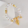Detail of elegant pearl bracelet with golden seashell charm and nautical accents - Conch