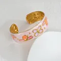 Gros plan d'un bracelet doré avec fleurs en émail coloré et texture marbrée - Orange
