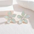 Dettaglio macro di orecchini a fiore in smalto bianco con bordi dorati e zircone - Blu